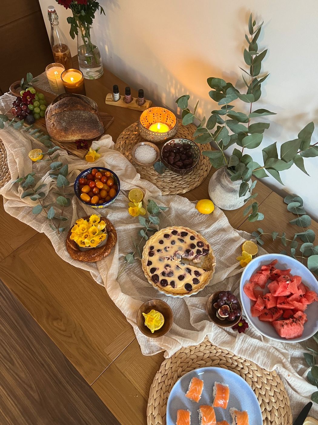 A shared table with fruit, bread, flowers and candlelight